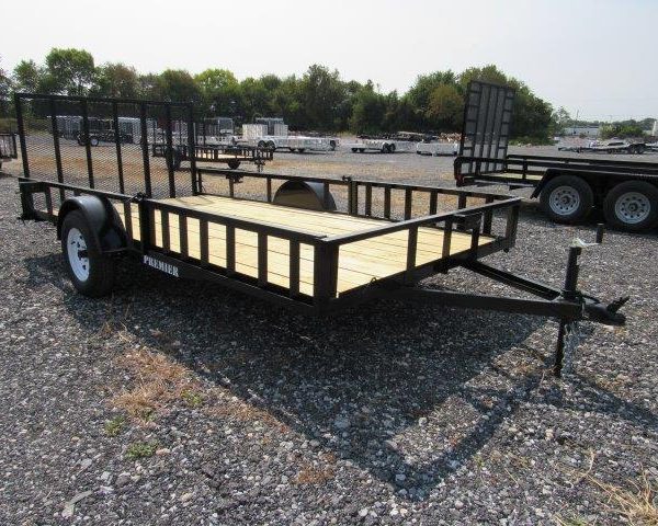 a trailer with a wooden deck is parked in a gravel lot .