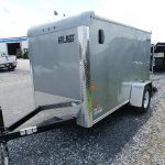 a gray trailer parked on a gravel road next to a truck