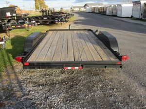 a trailer with a wooden deck is parked in a gravel lot