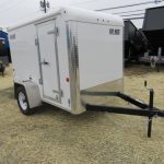 a white trailer is parked in a field of hay .