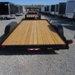 a trailer with a wooden deck is parked in a gravel lot .