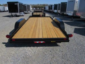 a trailer with a wooden deck is parked in a gravel lot .