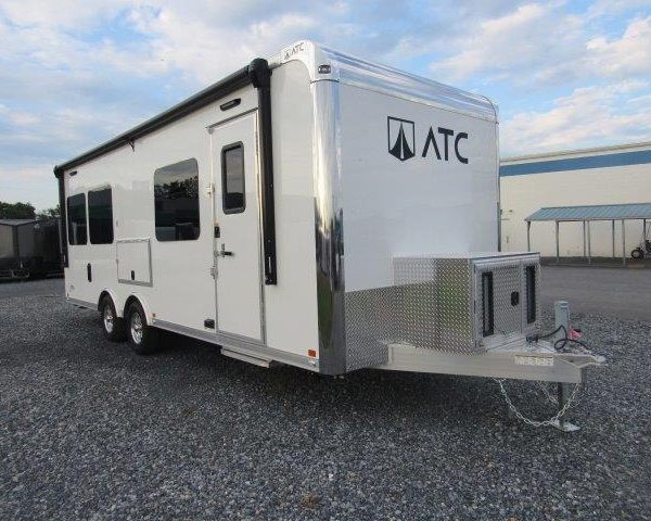 a white trailer is parked in a gravel lot in front of a building .
