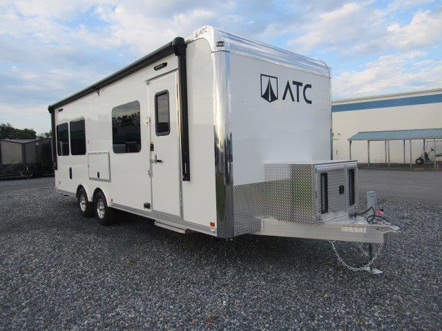 a white trailer is parked in a gravel lot in front of a building .