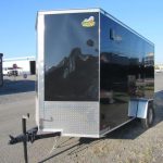 a black and silver trailer is parked in a gravel lot .