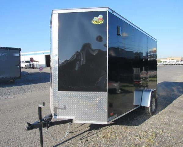 a black and silver trailer is parked in a gravel lot .