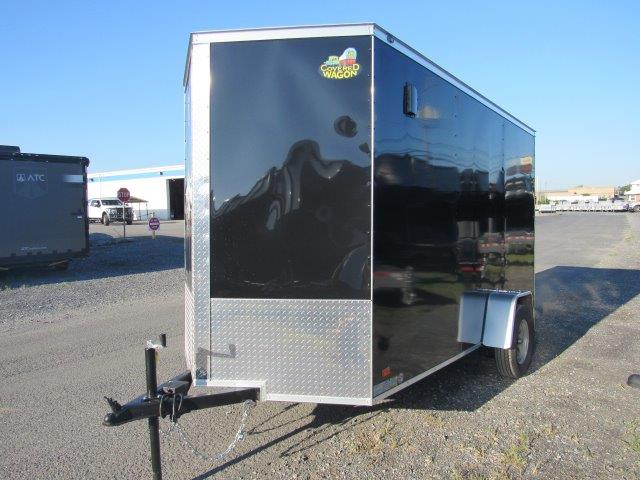 a black and silver trailer is parked in a gravel lot .