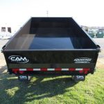a cam dump trailer is sitting on top of a lush green field .