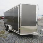 a black and silver trailer is parked in a gravel lot .