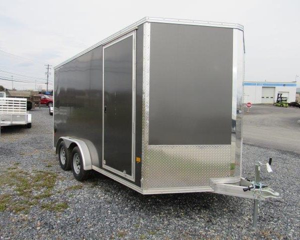 a black and silver trailer is parked in a gravel lot .