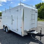 a white trailer with a ladder attached to it parked in a gravel lot