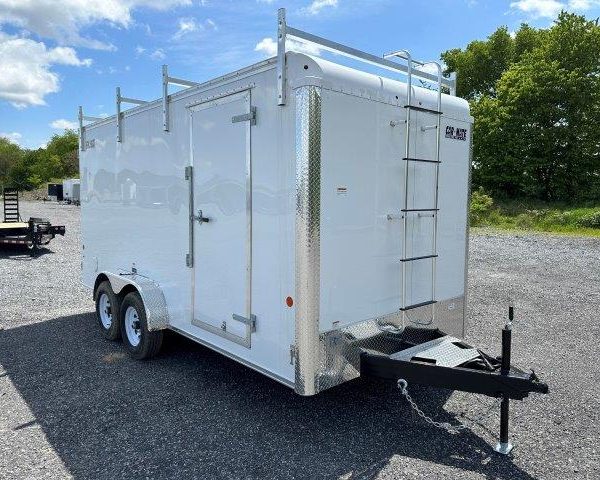 a white trailer with a ladder attached to it parked in a gravel lot
