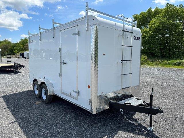 a white trailer with a ladder attached to it parked in a gravel lot