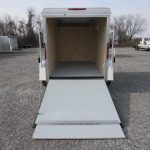 a white trailer with the door open is parked in a gravel lot