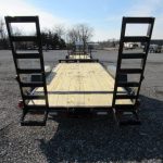 a wooden trailer with ladder ramps is parked in a gravel lot .
