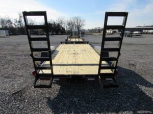 a wooden trailer with ladder ramps is parked in a gravel lot .