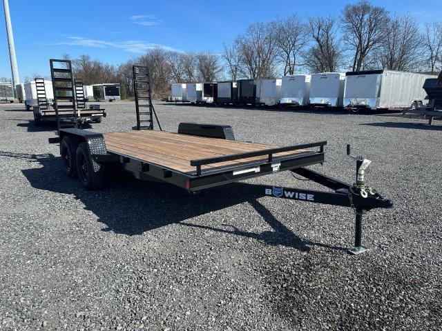 a trailer with a wooden deck is parked in a gravel lot .