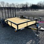 a small trailer with a wooden deck is parked in a gravel lot .