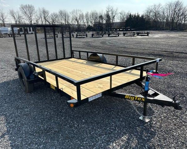 a small trailer with a wooden deck is parked in a gravel lot .