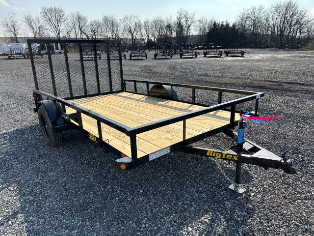 a small trailer with a wooden deck is parked in a gravel lot .