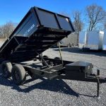a black dump trailer parked in a gravel lot