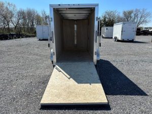 an empty cargo trailer is parked in a gravel lot .
