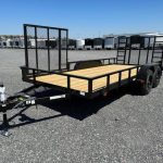 a carry on trailer with a wooden deck is parked in a gravel lot .