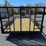 a carry on trailer with a gate it is parked in a gravel lot .