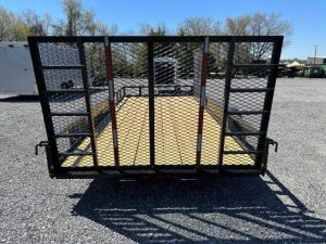 a carry on trailer with a gate it is parked in a gravel lot .