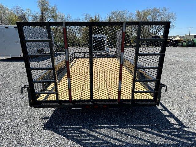a carry on trailer with a gate it is parked in a gravel lot .