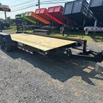 a CAM Superline flatbed trailer with a wooden deck parked next to a row of dump trailers