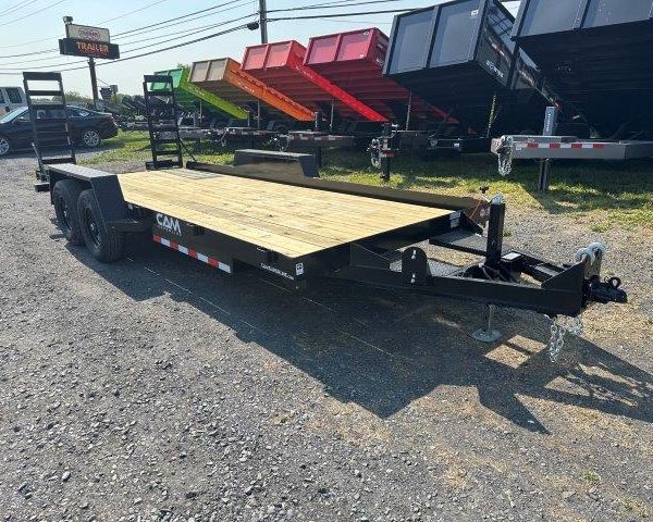 a CAM Superline flatbed trailer with a wooden deck parked next to a row of dump trailers