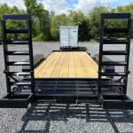 a trailer with a wooden deck is parked in a gravel lot .