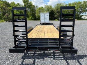 a trailer with a wooden deck is parked in a gravel lot .