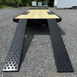 a flatbed trailer with ramps attached to it is parked in a gravel lot