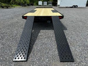 a flatbed trailer with ramps attached to it is parked in a gravel lot