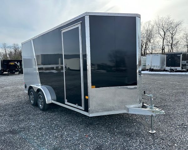 a black and silver trailer is parked in a gravel lot