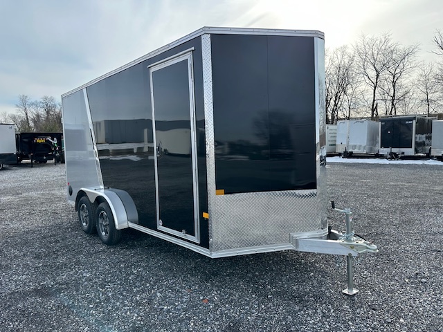 a black and silver trailer is parked in a gravel lot