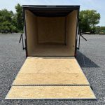an empty covered wagon trailer is sitting in a gravel lot .