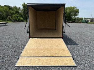 an empty covered wagon trailer is sitting in a gravel lot .
