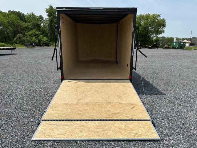 an empty covered wagon trailer is sitting in a gravel lot .