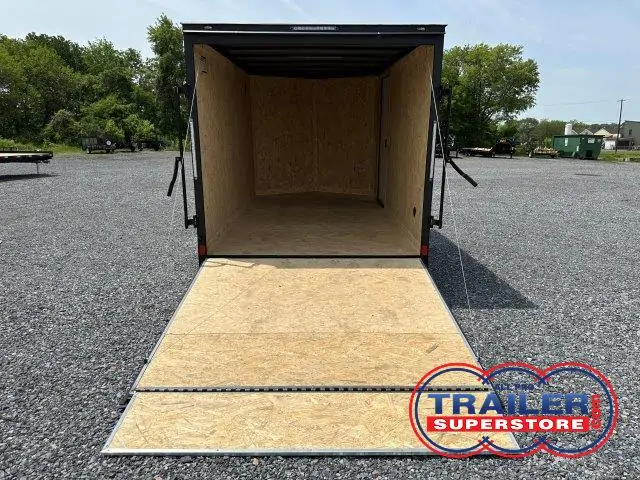 an empty covered wagon trailer is sitting in a gravel lot .
