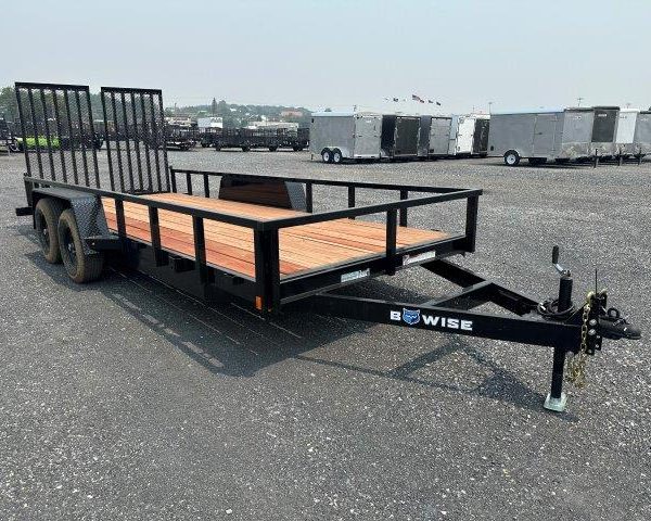 a black trailer with a wooden deck parked in a gravel lot
