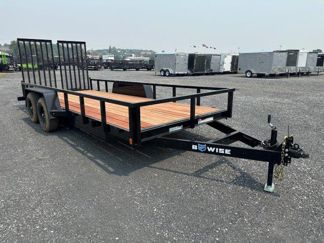 a black trailer with a wooden deck parked in a gravel lot