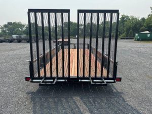 a bwise trailer with a wooden deck parked in a gravel lot .