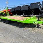 a green trailer is parked in a dirt lot next to a row of dump trailers