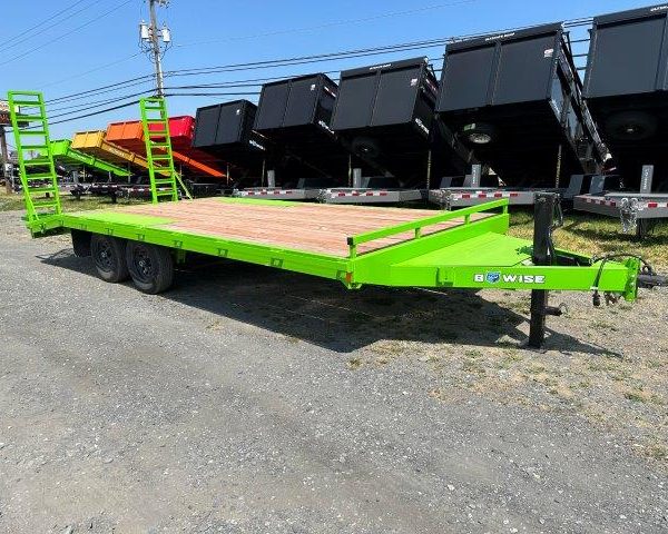 a green trailer is parked in a dirt lot next to a row of dump trailers
