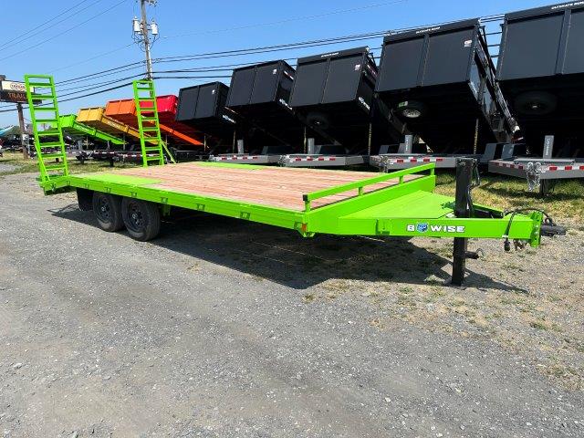 a green trailer is parked in a dirt lot next to a row of dump trailers
