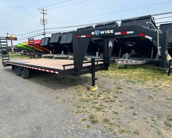 a black flatbed trailer is parked in a gravel lot .