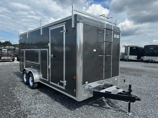 a black trailer with a ladder parked in a gravel lot